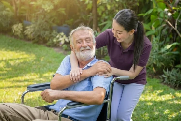 Pflegeschwester hält die Hand eines älteren Mannes in einem Garten