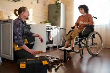 Ein Klempner repariert die Spüle bei einer Frau im Rollstuhl